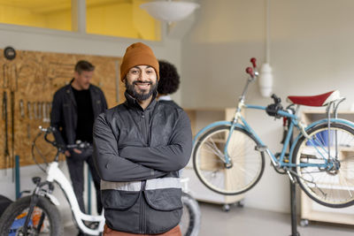 Portrait of happy male worker with arms crossed during cycle repairing workshop at recycling center