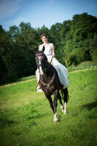 Bride riding horse on grassy field