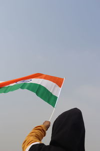 Low angle view of hand holding flag against sky