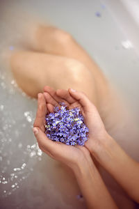 Woman is lying in the bath with water in the spa and holds small blue forget-me-nots in her hands