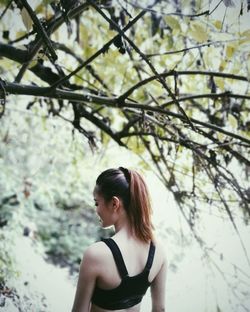 Woman looking away while standing against tree