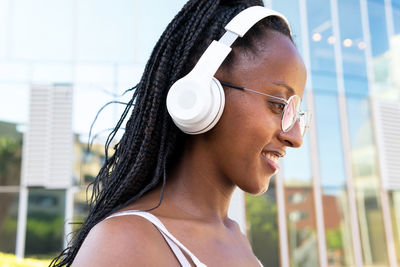 Positive african american female in headphones sitting in street in barcelona and enjoying songs while looking away