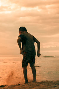 Rear view of boy jumping on beach during sunset