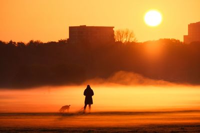 Silhouette man on shore against sky during sunset