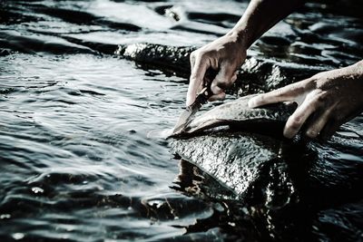 Cropped hand cutting fish on rock by lake
