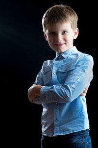 Portrait of boy standing against black background