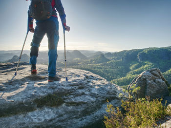 Man tourist with fixed leg makes step on rocky hill with help of forearm crutches.