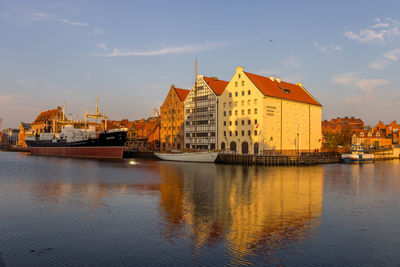 Boats moored on river by buildings in city against sky