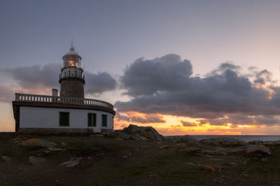 Lighthouse by building against sky during sunset