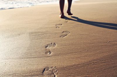 Low section of person walking on shore at beach leaving behind footprints