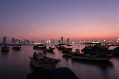 River by illuminated city against clear sky during sunset