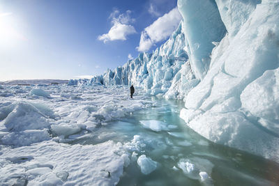 Back view of unrecognizable traveler hiker admiring spectacular scenery of frozen seashore with ice and snow in winter in iceland