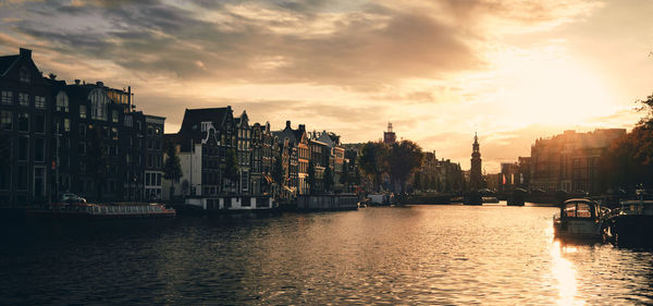 View of buildings by river against cloudy sky