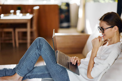 Young woman using laptop while sitting on sofa at home