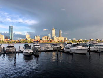 Boats moored in river by buildings against sky in city