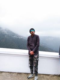 Portrait of young man standing on mountain against sky