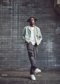 Portrait of young man standing against brick wall