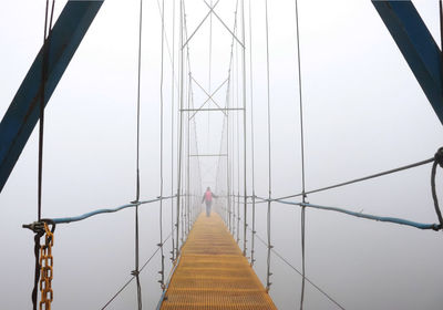 Rear view of woman walking on footbridge against sky