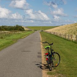 Bicycle on road amidst field against sky