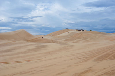 View of sand dunes in desert against cloudy sky