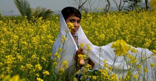 Young woman standing by yellow flowers on field