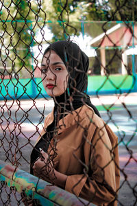 Portrait of young woman standing by fence