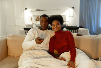 Young african couple relaxing sofa under blanket at home, biracial man and woman watch tv together