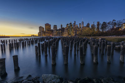 Wooden posts in river against sky at sunset