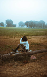 Rear view of woman sitting on field against sky