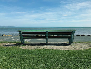 Empty bench by sea against sky