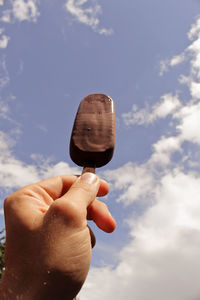 Cropped hand of man holding ice cream against sky