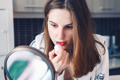 Close-up of woman applying lipstick while looking in mirror