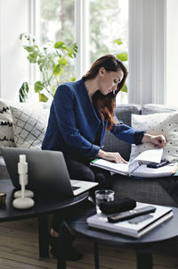 Businesswoman reading document while sitting on sofa at home office