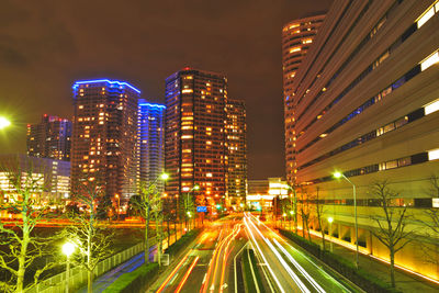 Light trails on road amidst buildings against sky at night