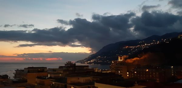 Buildings by sea against sky during sunset