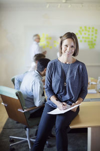 Portrait of confident businesswoman in conference room with colleagues discussing in background