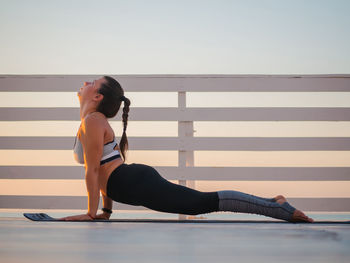 Full length of woman doing yoga on promenade during sunrise