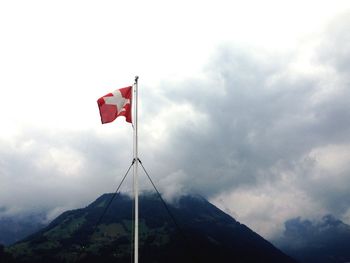 Low angle view of red flag against cloudy sky