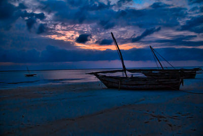 Boat moored on beach against dramatic sky