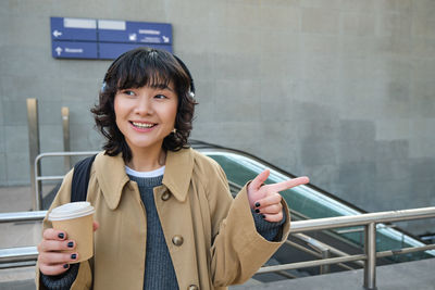 Portrait of smiling young woman standing against wall