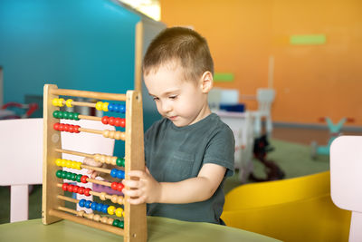 Cute toddler boy playing with colourful toy abacus in a children's entertainment center