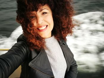 Portrait of smiling young woman with curly hair by sea