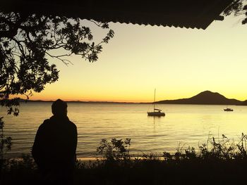 Silhouette man fishing in lake against sunset sky