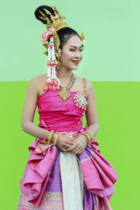 Smiling young woman wearing traditional clothing against wall