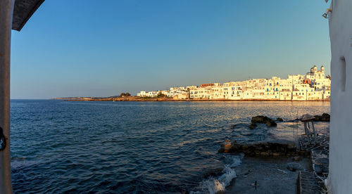 Buildings by sea against clear blue sky