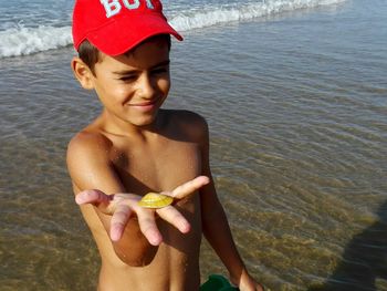 Smiling shirtless boy showing seashell at beach