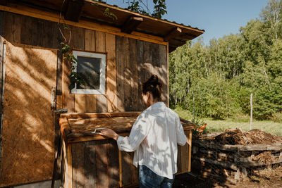 Morning routine on the farm, woman looks into the chicken coop to collect eggs