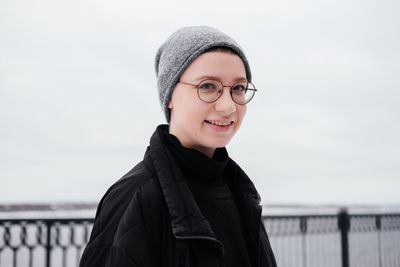 Portrait of a smiling young woman with short hair in hat, eyeglasses, black coat looking at camera