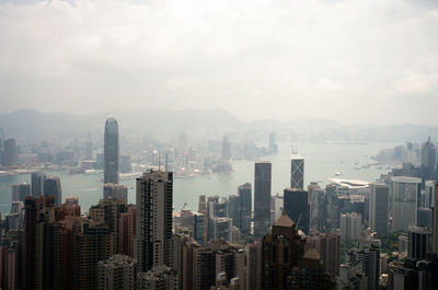 Cityscape at victoria harbour against sky during foggy weather