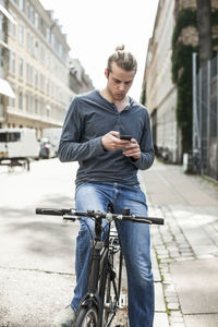 Young man using mobile phone while sitting on bicycle at street